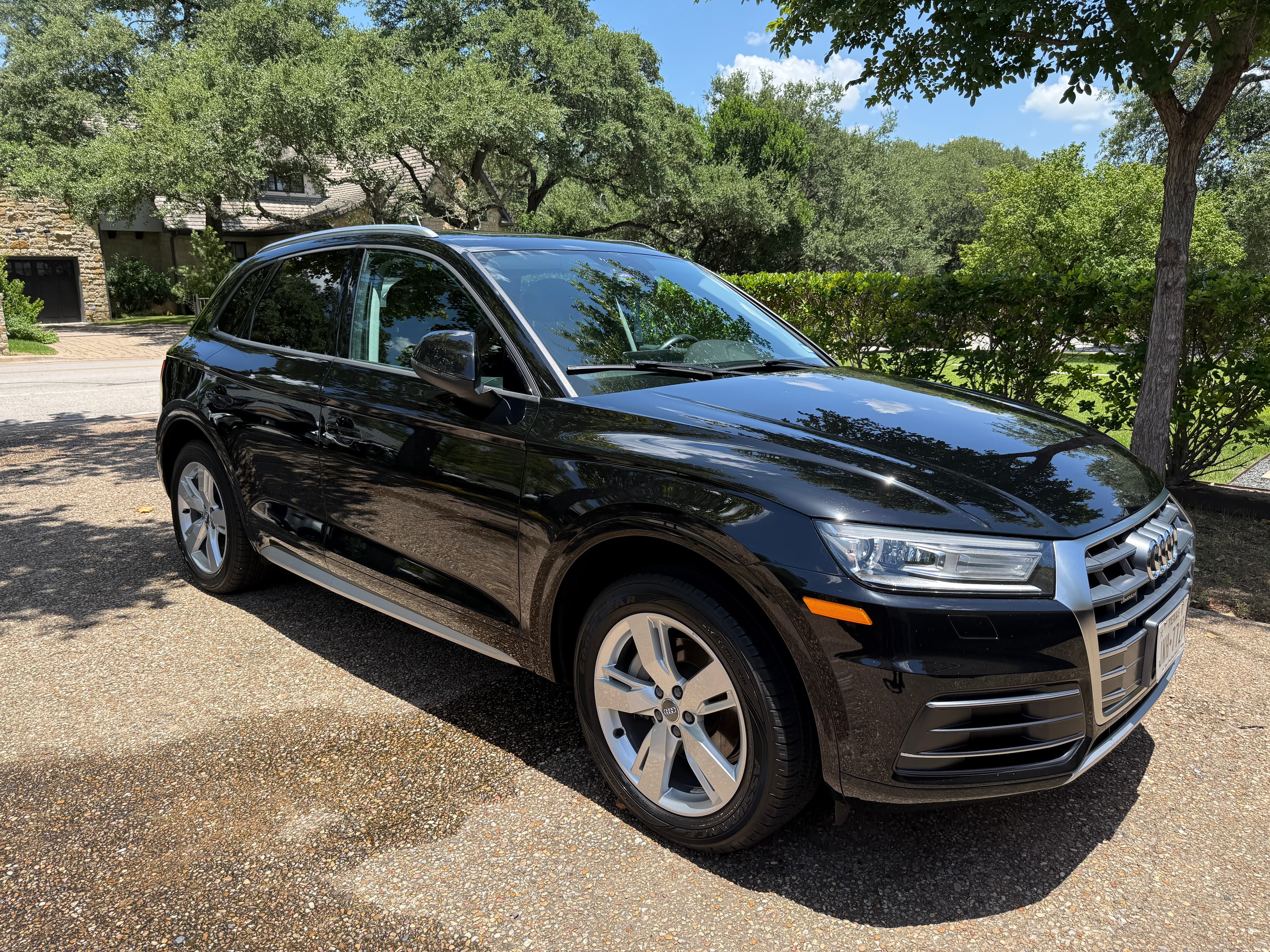 A shiny black Audi SUV parked on a gravel driveway surrounded by lush green trees.