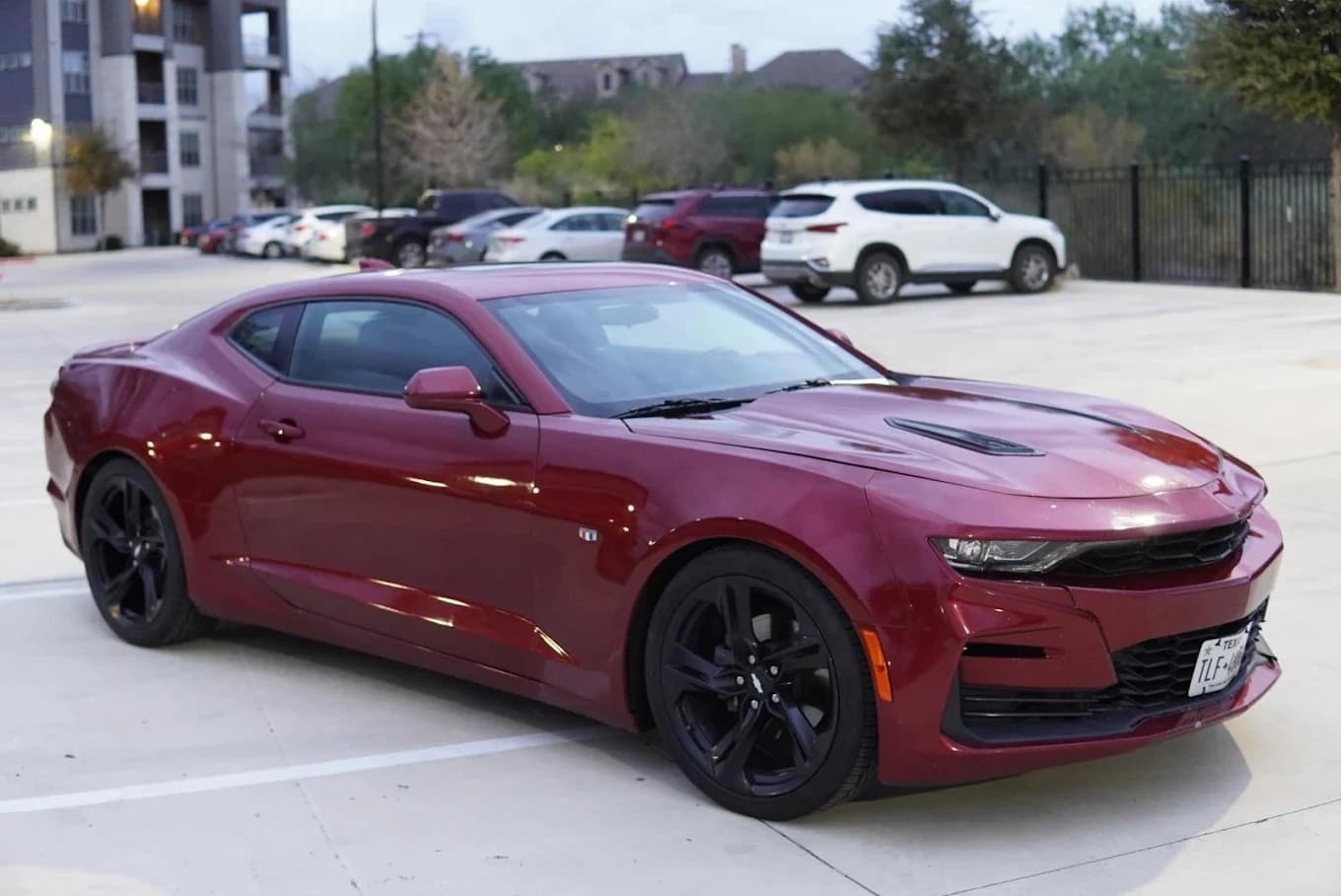 Maroon Chevrolet Camaro with black rims parked in a concrete lot with other cars.
